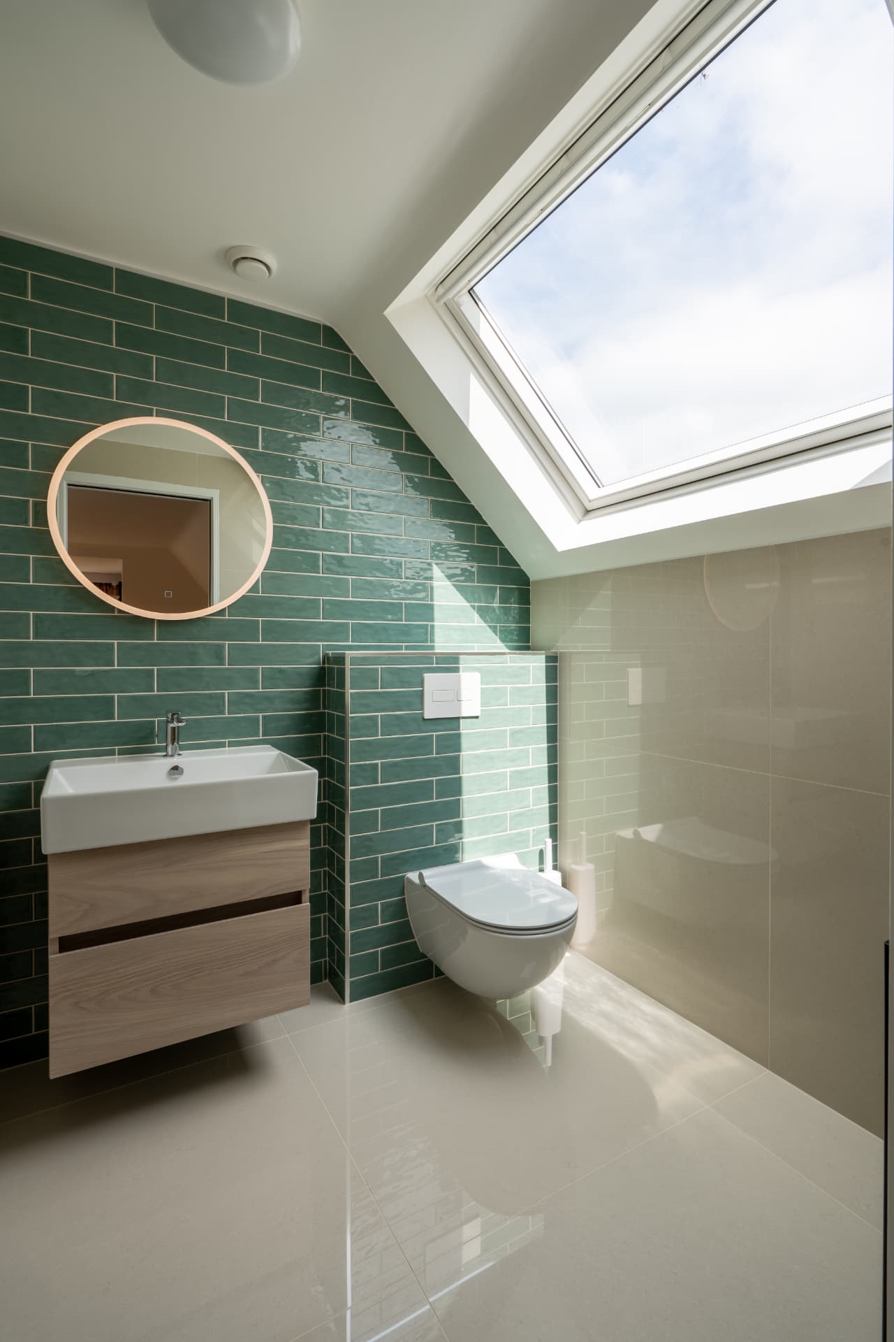 A loft shower room with green tiling beneath a pitched rooflight