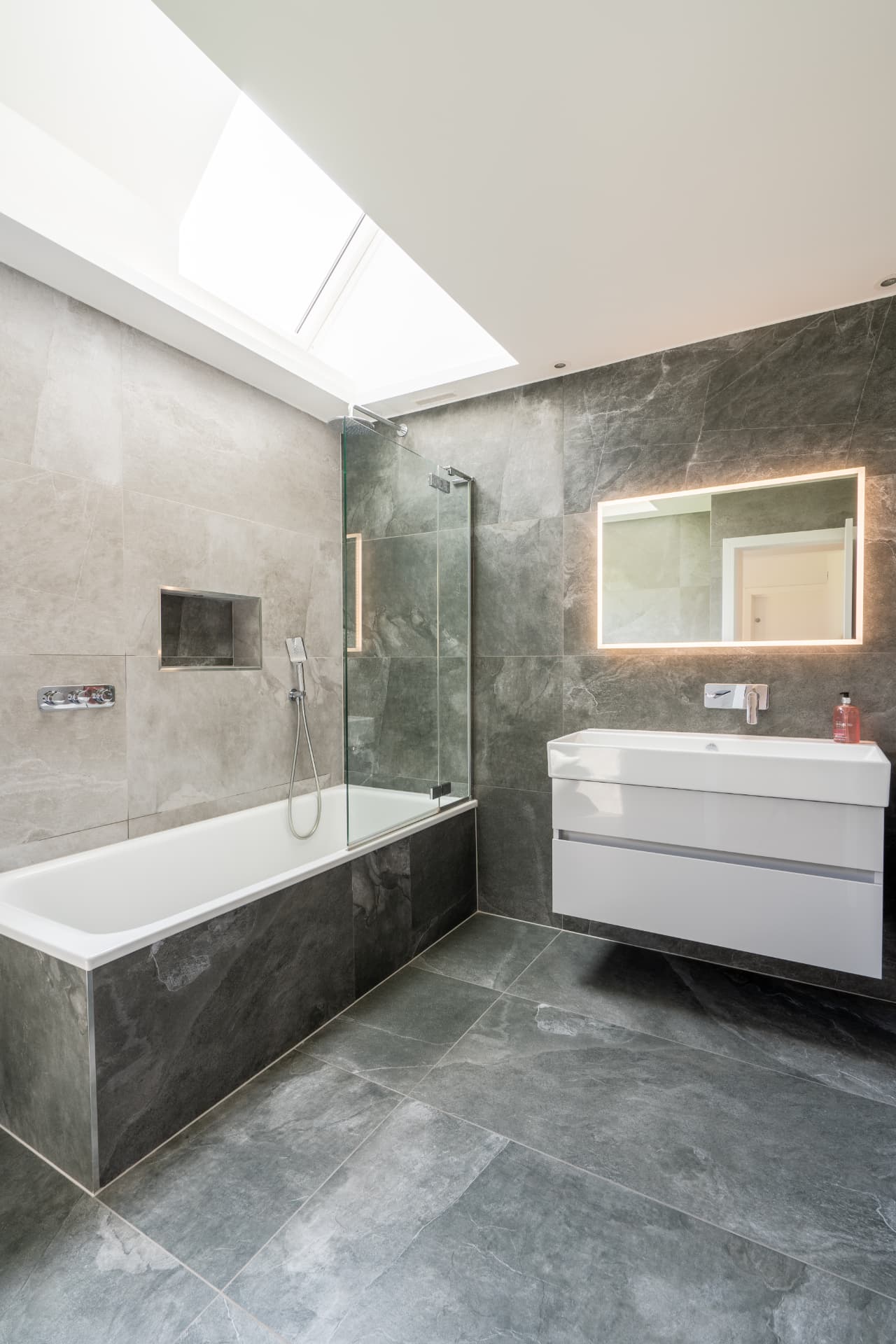 A completed bathroom with stone tiling and a rooflight above the bath