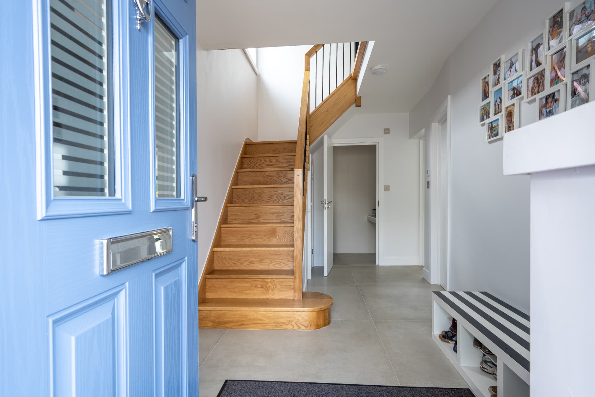 An open blue front door looking into a finished hallway with an oak staircase